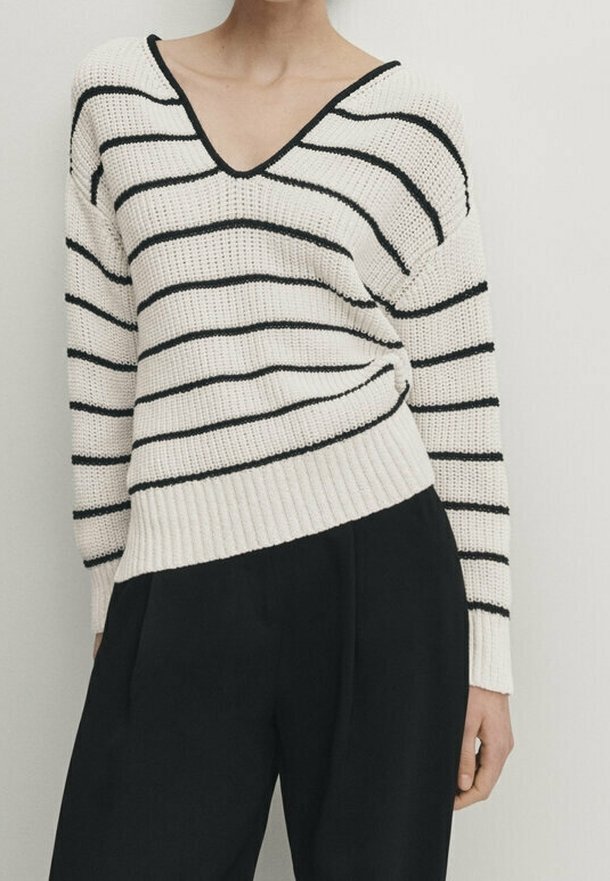 Pull en maille blanche avec des rayures horizontales noires, col en V, ourlet côtelé et coupe ample, associé à un pantalon noir.