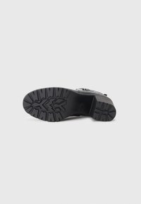 Black shoe sole with deep traction patterns, rubber material, and a chunky design. Features a textured upper for stability and grip.