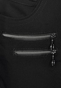 Svart tyg med två parallella dragkedjefickor. Dragkedjorna har silverfärgad hårdvara och är placerade på högra sidan, ovanför en slät yta.