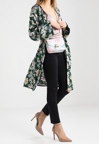 Grüner floral bedruckter Kimono über einem hellen Oberteil, kombiniert mit schwarzen, zerrissenen Skinny Jeans und beigen High Heels. Kleine Umhängetasche mit floralem Muster.