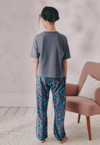 Graues, kurzärmliges T-Shirt mit lockerer Passform, kombiniert mit blau gemusterten Schlafanzughosen, die Cartoon-Figuren auf einem strukturierten grauen Stoff zeigen.