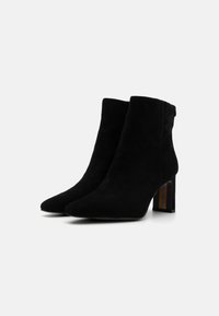 Botas de tobillo de ante negro con punta afilada y tacón cuadrado, que cuentan con un acento multicolor. Textura suave, silueta elegante.