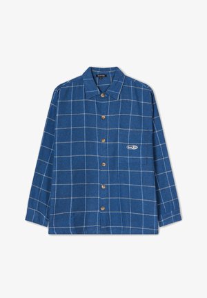Camisa de franela a cuadros en azul, con mangas largas, frente abotonado, cuello puntiagudo y un pequeño logo en el bolsillo del pecho.