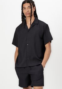 Sorte kortærmede skjorte med krave, der har et struktureret ribbet design og knapper, parret med matchende ribbet shorts.