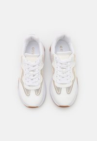 Białe sportowe sneakersy z siateczkową tkaniną, złotymi i beżowymi akcentami oraz teksturowaną podeszwą. Posiadają płaskie sznurowadła i wyściełany kołnierz dla wygody.