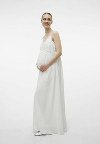 Robe blanche maxi longueur avec un bodice en dentelle délicate et des bretelles réglables ; tissu doux et fluide ; sandales argentées visibles aux pieds.