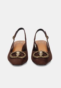 Zapatos de tacón en ante marrón con combinación de tiras, punta cuadrada, que presentan una hebilla decorativa en tono dorado y un acento de gema en la parte superior. Plantilla de cuero suave.