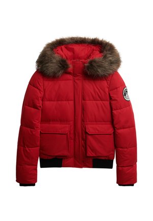 Rød puffjakke med hætte med pelskant, lynlåslukning og to forreste påsyede lommer. Har ribbede sorte manchetter og et rundt logo-patch på ærmet.