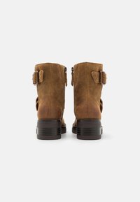Brown suede ankle boots with a rounded toe, black stacked heel, two adjustable straps with buckles, and a smooth, textured finish.