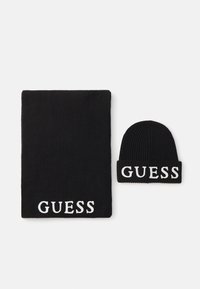 Juodas megztinis šalikas ir jam tinkantis kepurė, abu su balta "GUESS" logo. Minkšta tekstūra su raštuotais kraštais. Šalikas yra didesnis už kepurę.