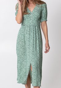 Green floral midi dress with a V-neck, short puff sleeves, button detailing, elastic waist, and a front slit for ease of movement.