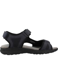 Sandalia negra con parte superior texturizada, punta abierta y correas ajustables; suela acolchada, diseñada para la comodidad y la estabilidad.