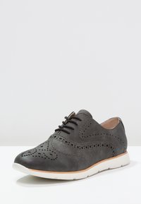 Chaussure oxford en cuir gris avec un design perforé, à lacets à l'avant, bout rond et semelle en caoutchouc blanc, présentant une texture lisse et des accents subtils.