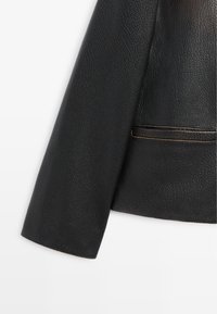 Manica di giacca in pelle nera strutturata con tasca orizzontale e cuciture visibili su sfondo bianco.