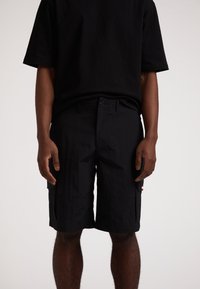 Schwarze Cargo-Shorts aus strukturiertem Stoff, mit Seitentaschen, einem Knopfverschluss und einem flachen Frontdesign. Arbeiterstil mit funktionalen Akzenten.