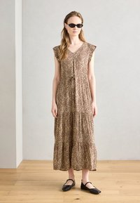 Hnědo-bežové maxi šaty s leopardím potiskem, s volánkovými rukávy, stahovacími šňůrkami v pase a s vrstveným designem; nošené s černými balerínami a slunečními brýlemi.