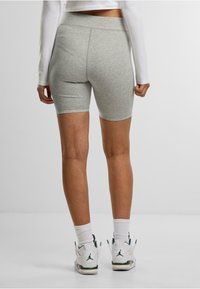 Shorts da biker in cotone grigio chiaro con vita alta, texture liscia e design aderente, abbinati a sneakers bianche e calzini sopra la caviglia.