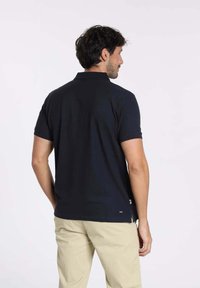 Polo bleu marine avec un col traditionnel, des manches courtes et un petit logo au bas. Tissu en coton lisse, coupe classique.