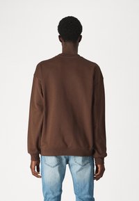 Felpa marrone con scollo a girocollo e maniche lunghe, con polsini e orlo a costine, abbinata a jeans blu chiaro.