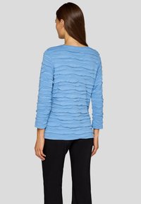 Helltürkises Oberteil mit einem strukturierten, wellenförmigen Design. Das Shirt hat lange Ärmel und eine lässige Silhouette, die durch einen Rundhalsausschnitt ergänzt wird.