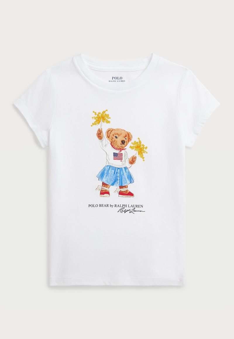 Bela bombažna majica z ilustracijo medveda v puloverju z ameriško zastavo, modri krilu in rumenimi pom-poni.