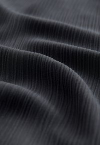 Tessuto nero texturizzato con costine verticali, che mostra un drappeggio ondulato e un aspetto morbido. Ideale per abbigliamento o tappezzeria.