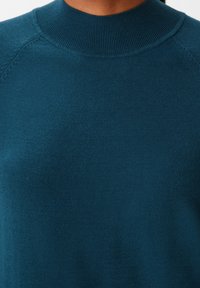 Maglione in maglia color teal con un collo alto a costine e una texture sottile. Il tessuto appare morbido e liscio, con una vestibilità aderente.