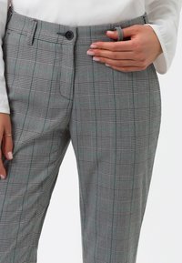 Grå rutig byxor med ett rutmönster, med en grön accentlinje, platt framsida och en enkel knappstängning.