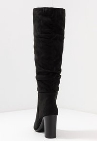 Botte haute jusqu'au genou en daim noir avec un design décontracté, un bout arrondi et un talon épais. Texture lisse et forme minimaliste.