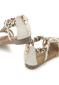 Helle beige Sandalen mit einer geflochtenen Blütenakzent, Reißverschluss am Knöchel, gepolsterter Innensohle und niedrigem Blockabsatz. Glatte Textur mit dezenten Details.