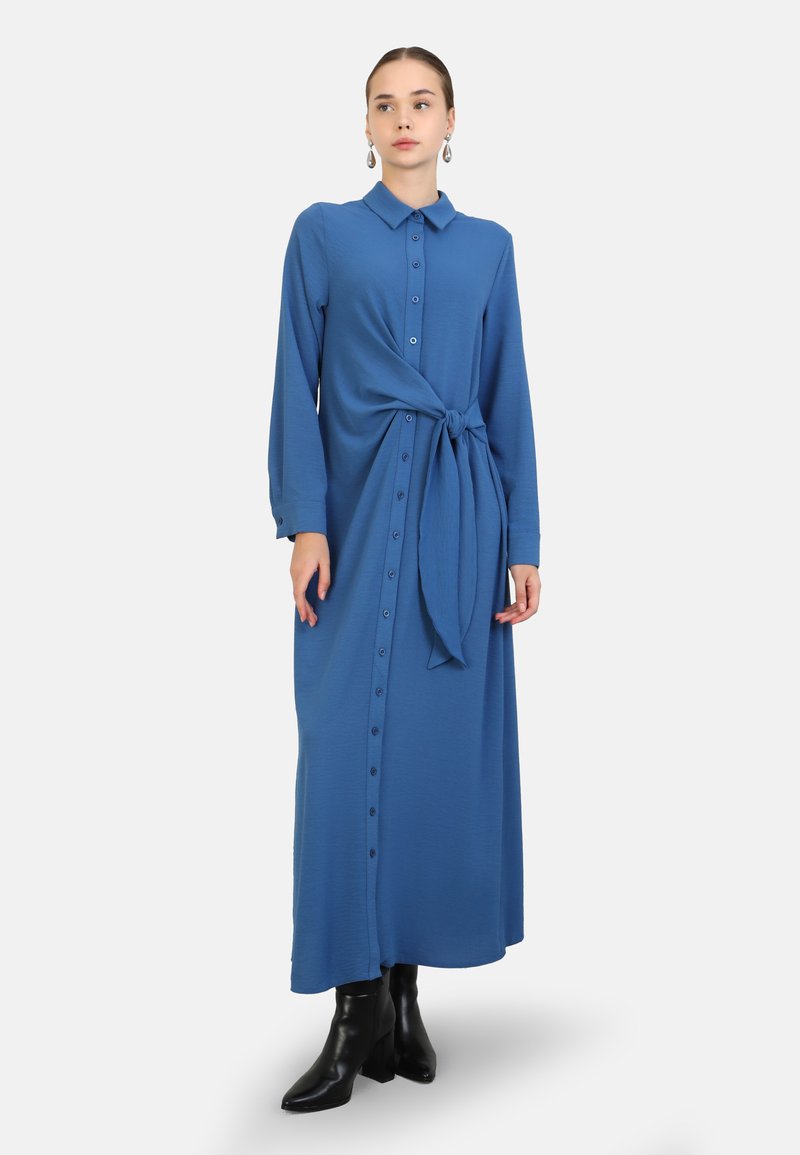Blue button-up maxi dress with long sleeves and a tie detail at the waist. Smooth texture, minimal hardware, and a relaxed silhouette.