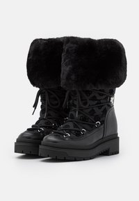 Stivali invernali neri con un risvolto in finta pelliccia, lacci frontali, parte superiore in nylon testurizzato con motivi logo e una suola in gomma spessa.