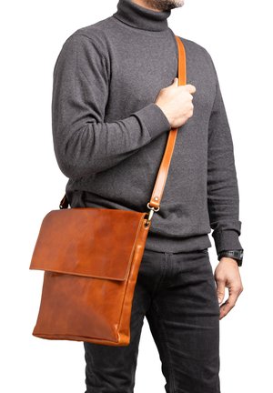 Bruine leren schoudertas met een klepsluiting en een verstelbare tan kleurige schouderband, kenmerkt zich door een gladde textuur en een minimalistisch design.