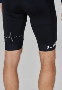 Pantaloni sportivi neri a vestibilità aderente, con un motivo a linea di battito cardiaco grigio e logo "LAB" in bianco sulla gamba inferiore. Texture liscia.
