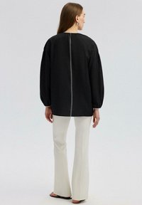 Top nero con collo alto, maniche a sbuffo e un dettaglio di cucitura bianca centrale sul retro, abbinato a pantaloni bianchi a campana.