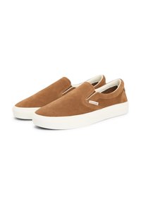 Paire de baskets marron en daim à enfiler avec semelles en caoutchouc blanches et petite étiquette en tissu sur le côté sur fond blanc.