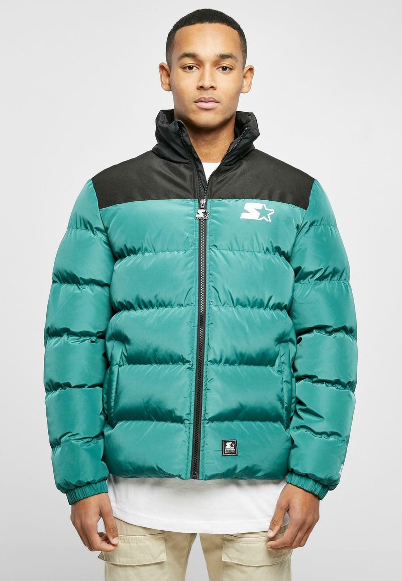 Teal puffer jacket with black shoulders, zip front, side pockets, and embroidered logo. Features a quilted design and elastic cuffs.