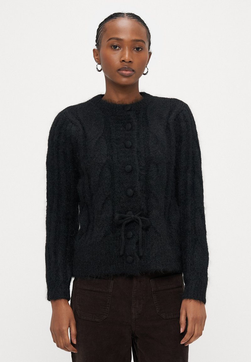 Μαύρο πουλόβερ ζακέτα με πλεκτό μοτίβο καλωδίου, στρογγυλή λαιμόκοψη, κουμπιά μπροστά και κορδόνι στη μέση. Διαθέτει μακριά μανίκια και υφασμάτινη υφή.