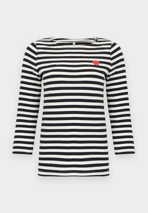 Μακρυμάνικο πουκάμισο με οριζόντιες ασπρόμαυρες ρίγες και μικρή λεπτομέρεια κόκκινης καρδιάς στο πάνω μέρος της αριστερής πλευράς του στήθους.