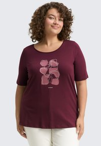 T-shirt bordeaux à manches courtes avec un col rond et un design d'art linéaire abstrait dans des nuances de rose sur le devant. Texture de tissu lisse.