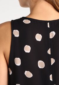 Top senza maniche di colore nero con motivi circolari beige, caratterizzato da un colletto pulito e una texture liscia e fluida del tessuto.