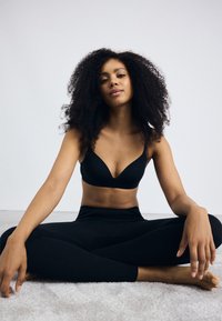 Black seamless sports bra with a V-neck design, paired with high-waisted black leggings. Smooth fabric with minimal hardware visible.