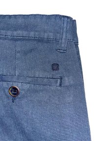 Pantalones de tela azul texturizada con un bolsillo trasero visible, botón en contraste y un pequeño parche con logo cerca de la cintura.