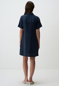 Robe bleu marine à manches courtes avec un col, taille cintrée et texture lisse, tombant juste au-dessus des genoux. Design simple et classique.