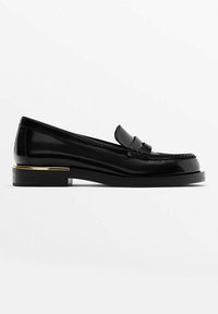 Mocassin en cuir noir avec un petit talon, un accent doré sur le talon, une tige cousue et un détail de bride sur le cou-de-pied.