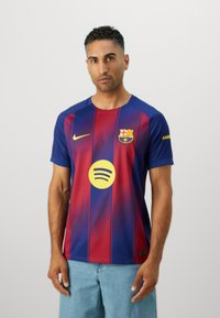 Tricoul FC Barcelona, cu dungi roșii și albastre, prezintă logo-ul Nike, logo-ul circular Spotify și un material texturat. Mâneci scurte și guler rotund.