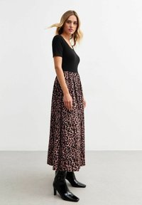 Leopard-print maxi dress with black fitted bodice and flowing skirt. High waist, short sleeves, and paired with black heeled boots.