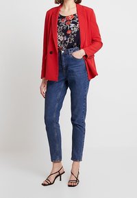 Červený blejzr s jedním knoflíkem, květinový vzorovaný námořnický top, džínové kalhoty s vysokým pasem a černé páskové podpatky. Hladký materiál a střih na míru.