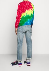 Tie-dye sweatshirt i röd, gul, grön och blå färg, parat med ljusblå jeans och blå sneakers med röda detaljer.