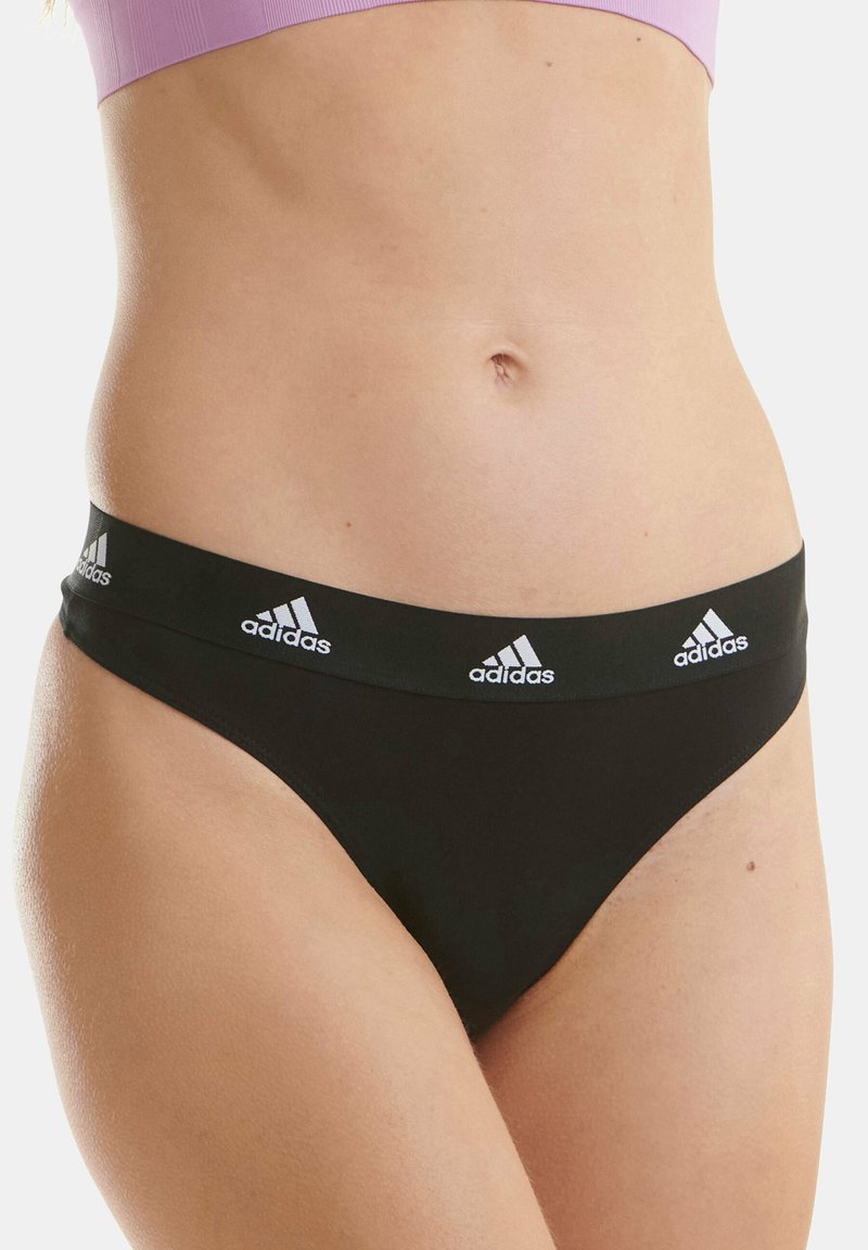 Schwarze Stringunterwäsche aus glattem Material, mit einem breiten elastischen Bund, der mit drei weißen Adidas-Logo-Akzenten verziert ist.